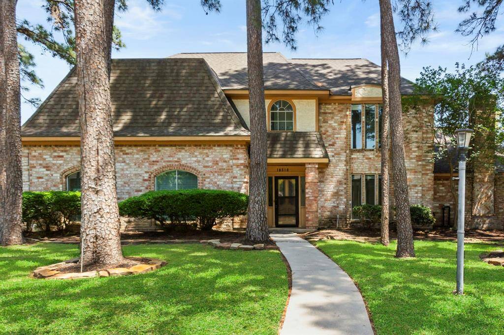 Charming two-story brick home with a welcoming front pathway, surrounded by mature trees and well-maintained landscaping. Large windows offer abundant natural light.