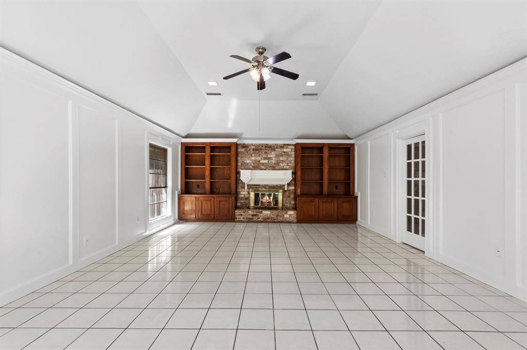 Spacious den features a central romantic brick fireplace, built-in wooden shelves, and large tile flooring.
