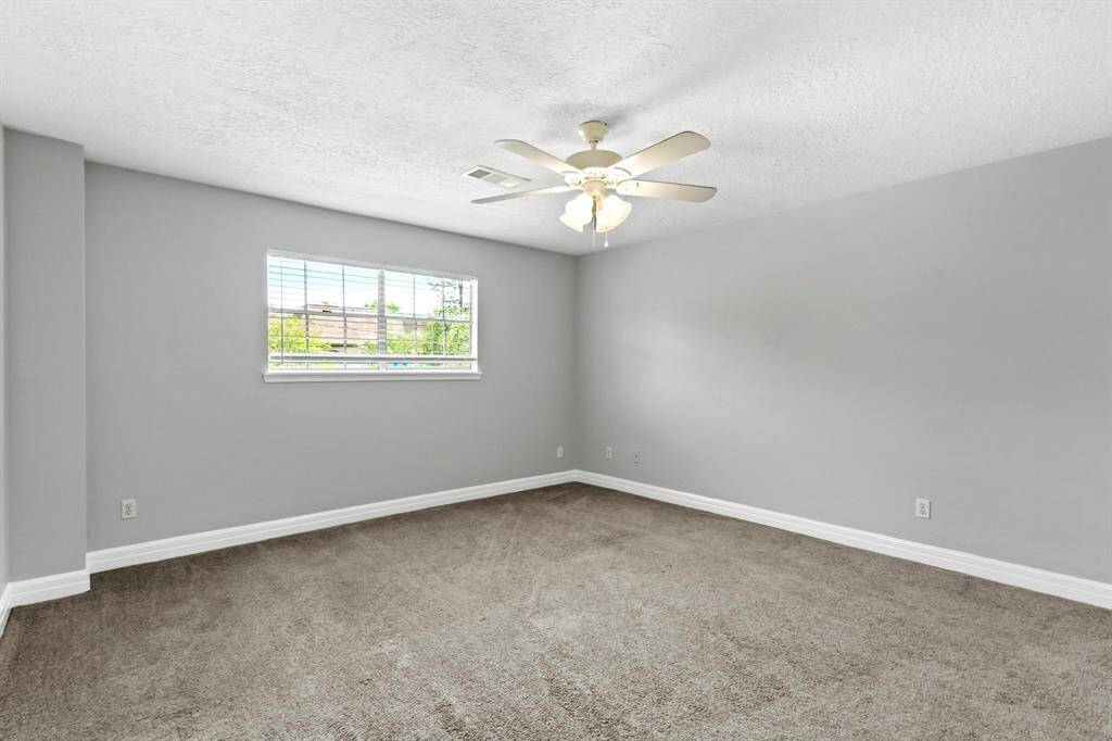 Fourth bedroom is spacious with neutral gray walls and carpeted flooring. It features a ceiling fan and a window providing natural light.