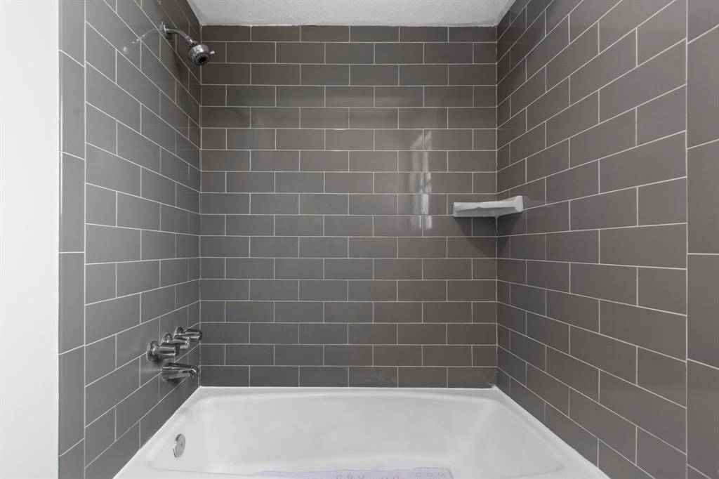 This photo shows a modern bathroom with a bathtub and sleek gray subway tile walls, featuring a built-in shelf and chrome fixtures.
