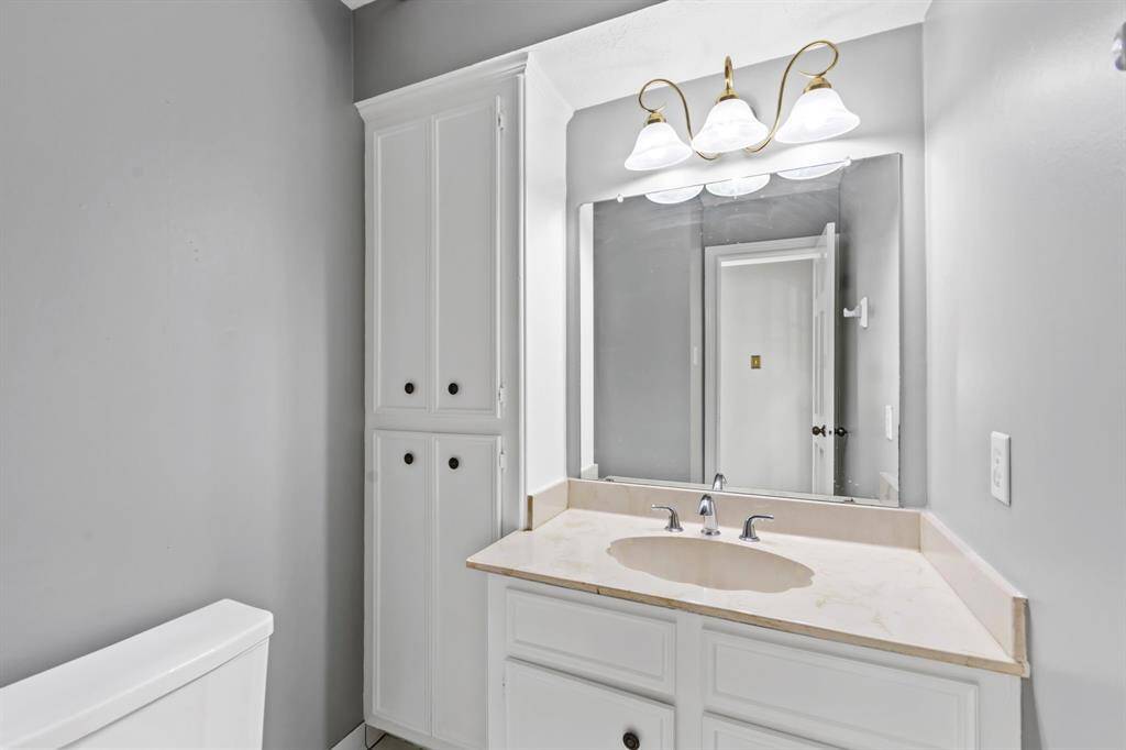 This bathroom features a sleek design with ample storage with cabinets, complemented by a large mirror and elegant overhead lighting. The neutral gray walls add a touch of sophistication.