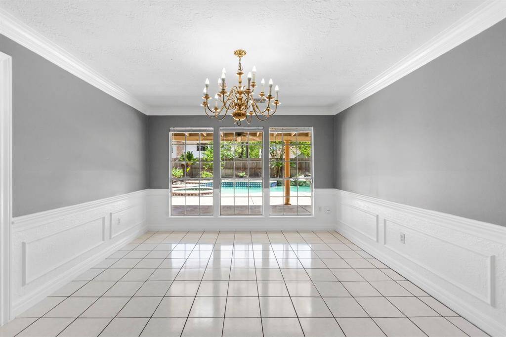 Bright dining room with elegant gray walls & tiled floors. Features a classic chandelier and large windows overlooking a pool.