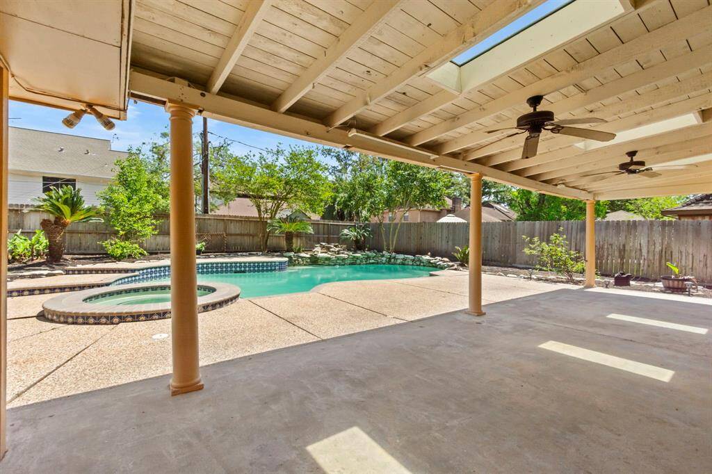 This outdoor space features a covered patio with ceiling fans, overlooking a spacious pool and spa. The backyard is fenced for privacy with lush landscaping, making it ideal for relaxation and entertaining.