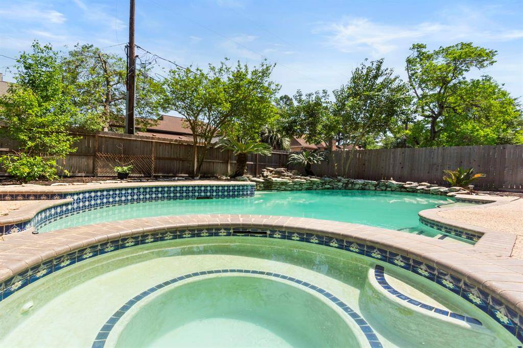 This photo showcases a private backyard oasis featuring a sparkling pool with a spa. Surrounded by lush greenery and a wooden fence, the space offers a serene and inviting atmosphere for relaxation and entertainment.