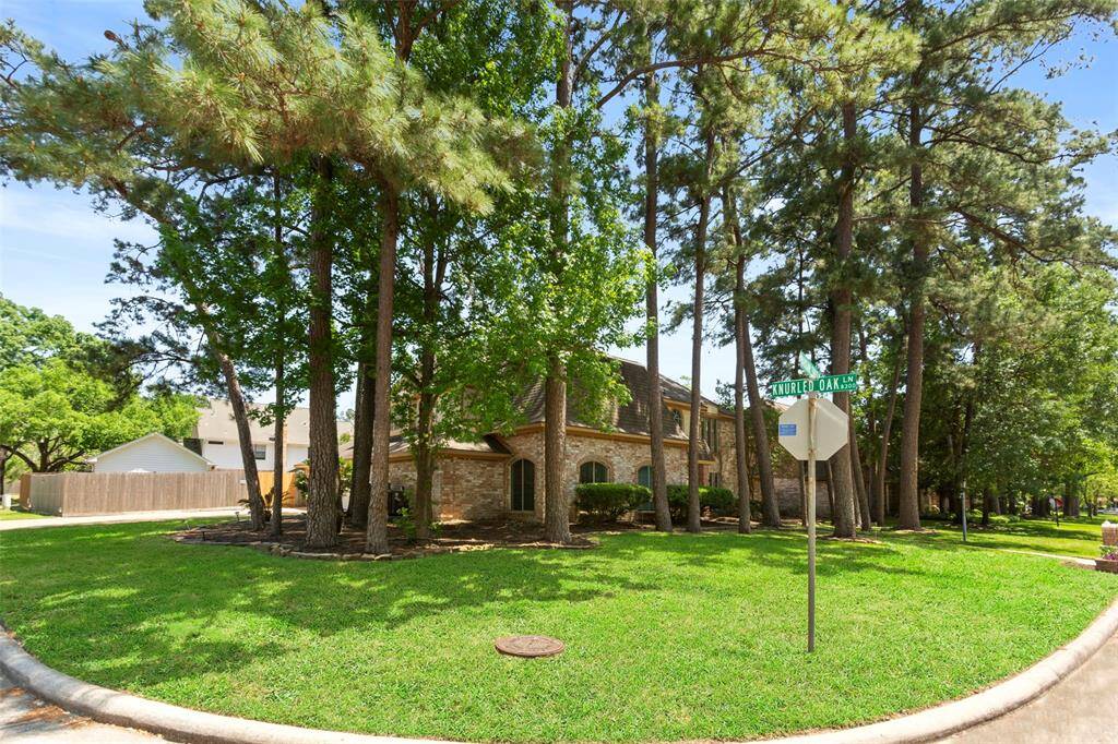 This corner property features a charming brick house surrounded by mature trees, providing ample shade and privacy. The well-maintained lawn adds to the curb appeal, located at the intersection of a quiet neighborhood street.