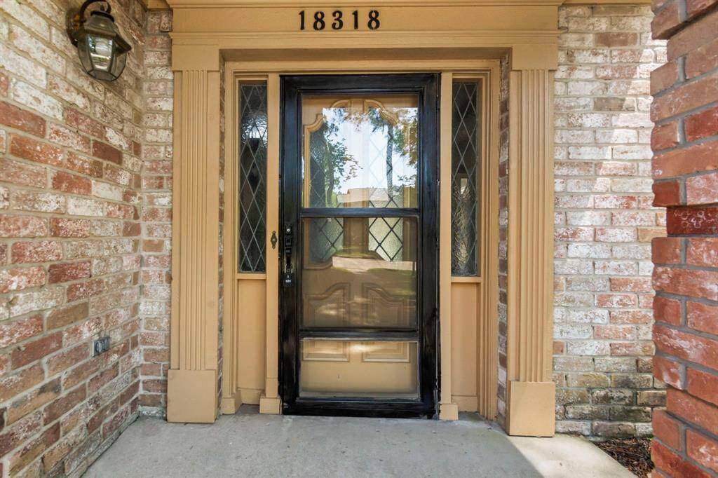 This photo shows a classic front entrance with a glass storm door. It features a brick exterior, a traditional porch light, and a welcoming atmosphere.