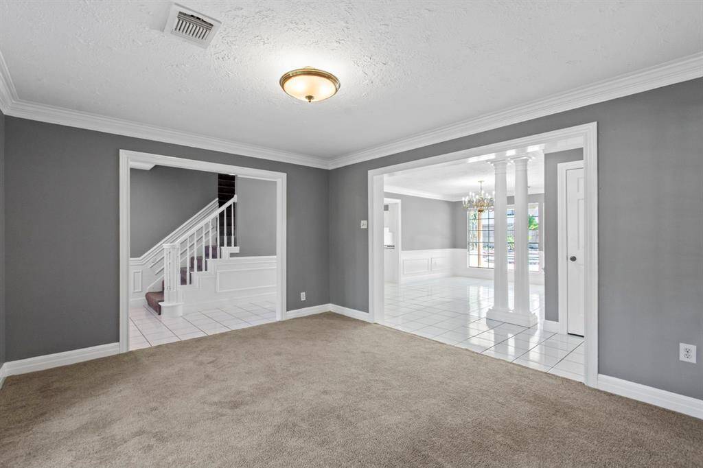 This photo shows a spacious, carpeted formal living room with gray walls, featuring white crown molding.