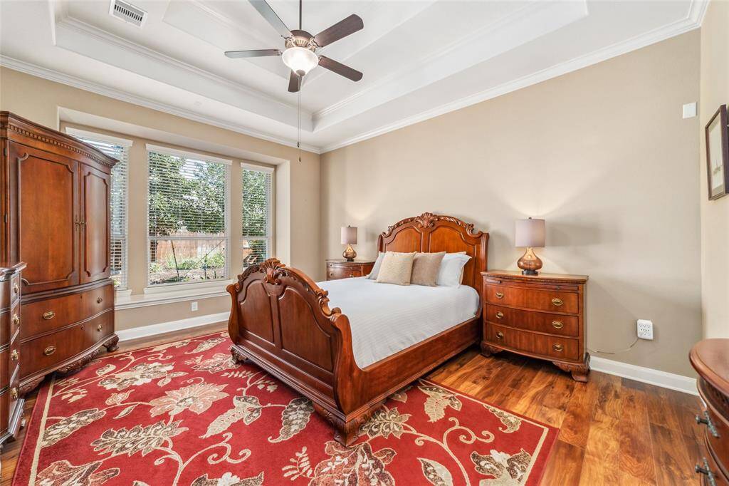 Gorgeous primary bedroom with tray ceilings, wood flooring, crown molding, window seat, and large windows looking out to your back yard oasis.