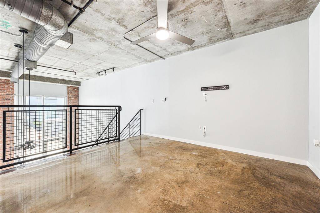 This industrial-style loft space features exposed ductwork, a concrete ceiling, and polished concrete floors. It has a modern railing overlooking a lower level, with large windows providing plenty of natural light. Perfect for a contemporary, open-concept design.