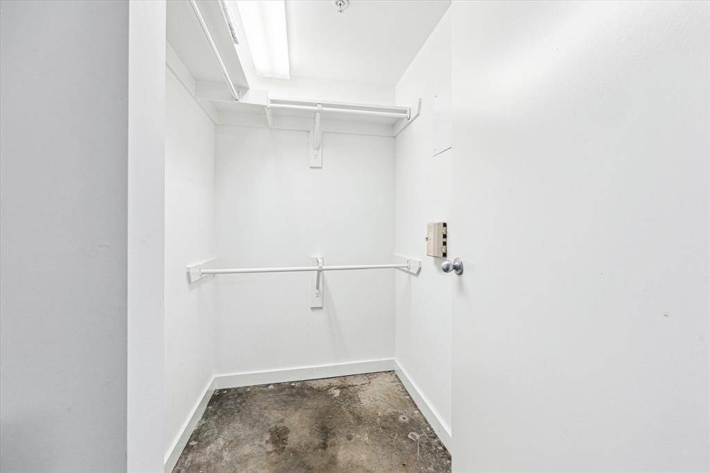 This photo shows a small, white walk-in closet with open shelving and hanging rods. The floor appears to be unfinished concrete, offering potential for customization.