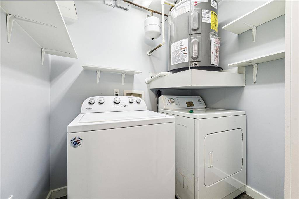 This photo shows a compact laundry room featuring a washer and dryer set, with a water heater mounted above. The room has several wall-mounted shelves for storage.