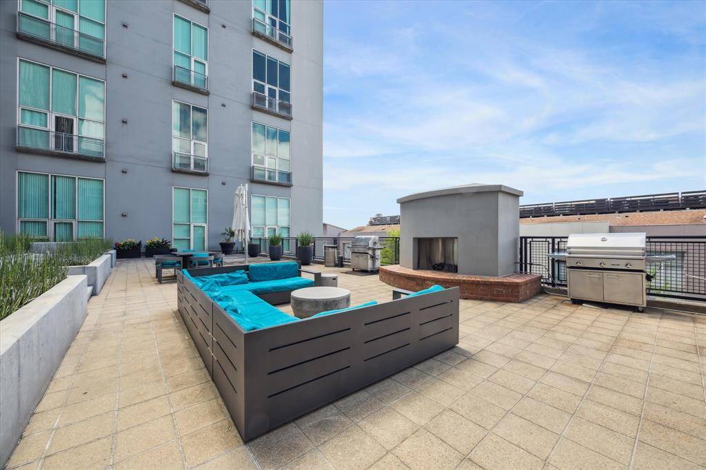 Spacious outdoor patio on a mid-rise building features modern seating, a cozy fireplace, and a built-in grill, perfect for entertaining and relaxation.