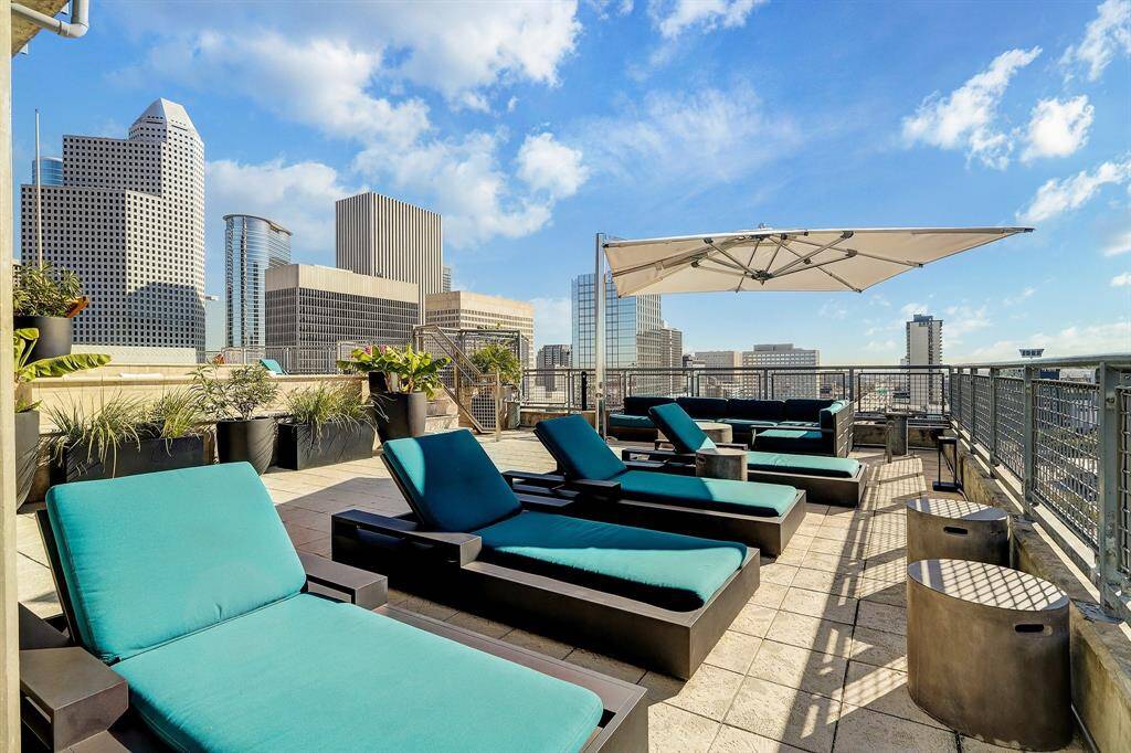 Spacious rooftop terrace with modern lounge chairs, large umbrella, and vibrant greenery, offering stunning city skyline views. Perfect for outdoor relaxation and entertaining.
