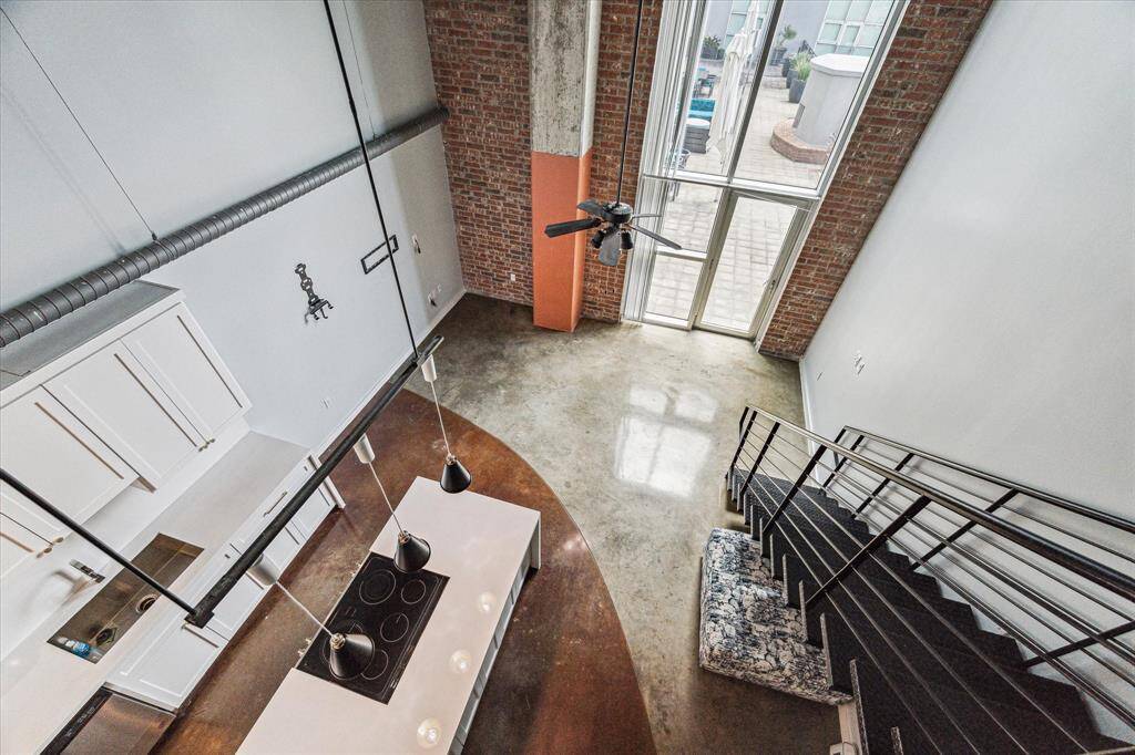 This modern loft features an open concept with high ceilings, large windows, and exposed brick for an industrial feel. The kitchen is equipped with sleek cabinetry and a central island. A stylish staircase leads to a mezzanine, enhancing the spaciousness. Perfect for contemporary living.