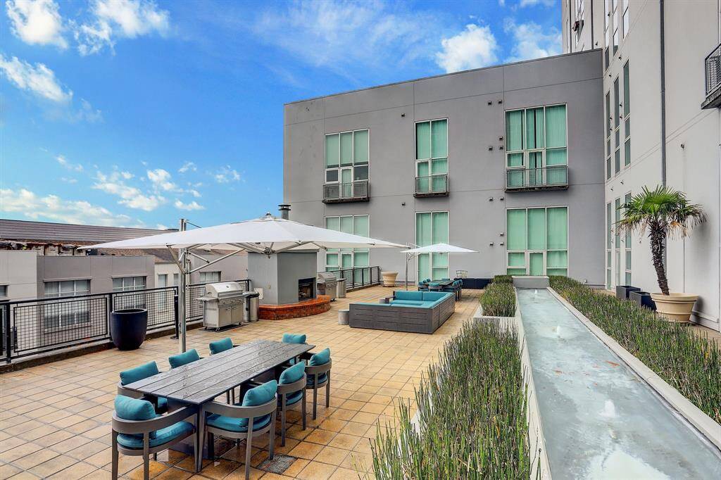 This photo showcases a modern rooftop patio with ample seating, shaded areas, a barbecue grill, and a water feature, ideal for outdoor entertaining.
