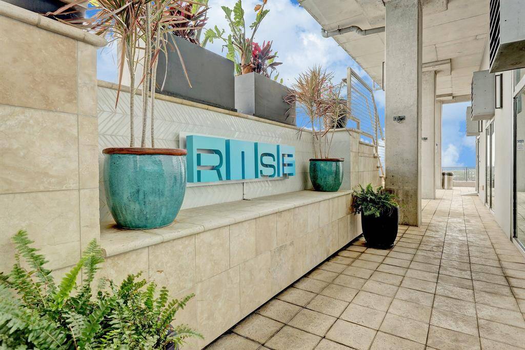 Modern outdoor terrace with stylish planters and sleek architectural design, featuring a sign that reads "RISE." Ideal for enjoying city views and relaxation.