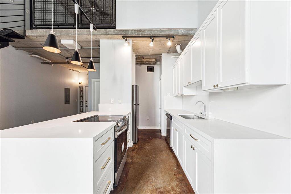 This modern kitchen features sleek white cabinetry, a spacious island with a built-in cooktop, and contemporary pendant lighting. The open layout and industrial elements, like exposed concrete and metal railings, create a stylish and functional space.