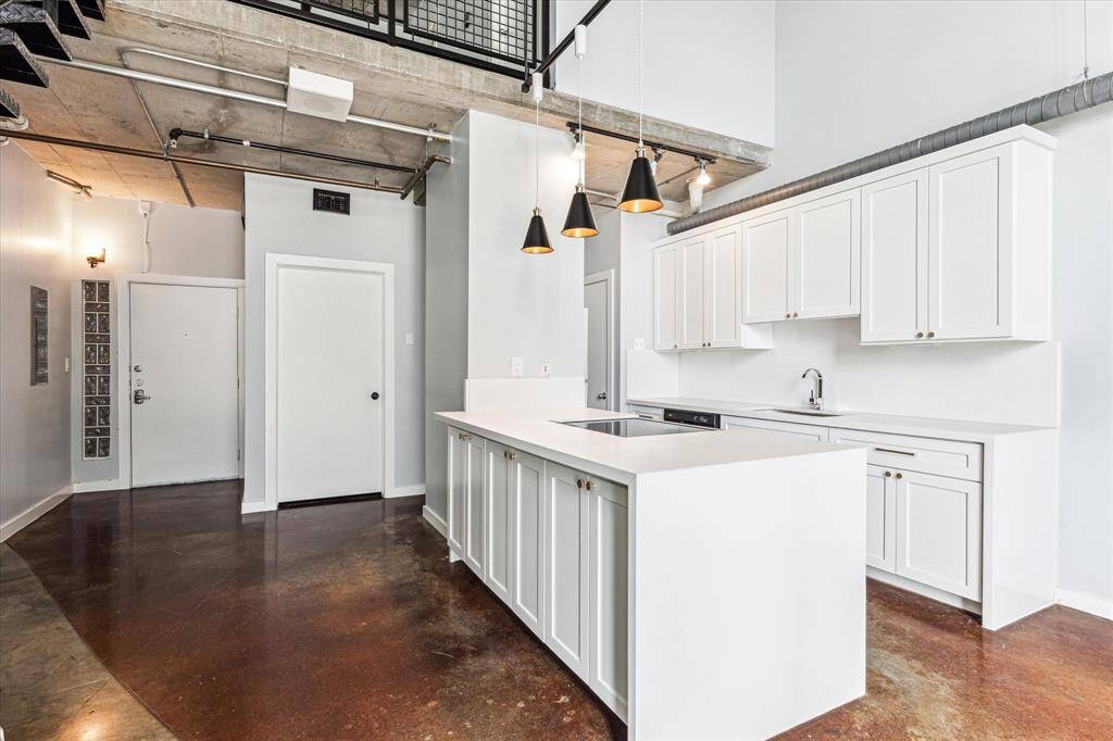 This photo showcases a modern kitchen with sleek white cabinetry, an island with a cooktop, and stylish pendant lighting. The open space features polished concrete floors and an industrial ceiling, offering a contemporary loft vibe.