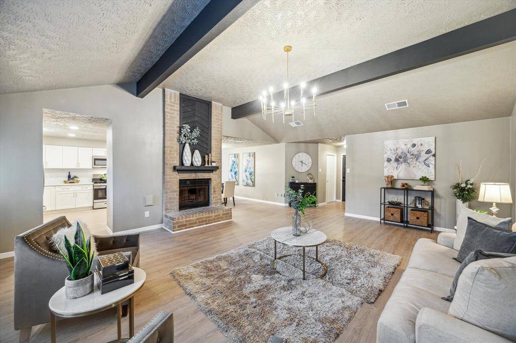 This beautifully designed living area offers a spacious layout with neutral tones and modern finishes. The vaulted ceiling, accented by dark beams, enhances the open feel. A glimpse into the bright, updated kitchen highlights the home’s seamless blend of style and functionality.