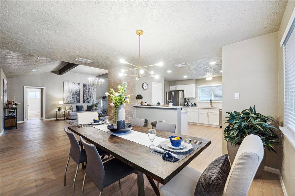 This open-concept layout seamlessly connects the kitchen, dining, and living areas for effortless flow. The modern kitchen with bar seating overlooks the spacious dining area, while the cozy living room sits just beyond the brick accent wall. Large windows and stylish lighting enhance the bright, inviting atmosphere.