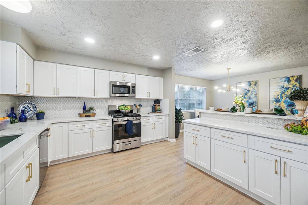 This elegant kitchen features crisp white cabinetry, gold hardware, and a stylish herringbone backsplash. Sleek quartz countertops provide ample prep space, while stainless steel appliances add a modern touch. The open design seamlessly connects to the dining area, perfect for entertaining.