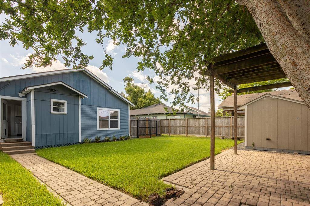 Large backyard with storage shed (with AC unit and power) and covered area with brick pavers.