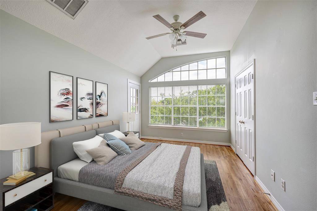 The third-floor guest bedroom features wood floors, vaulted ceilings, arched windows, and access to a covered balcony! Virtually staged photo.