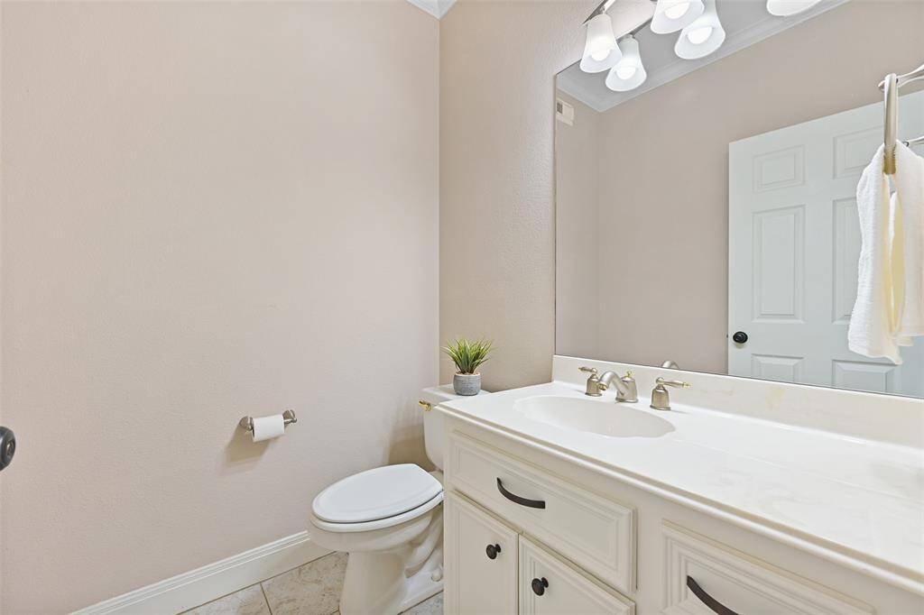 Located just off of the foyer, near the front door, there is a convenient half bathroom with tile floors, a cultured marble countertop and basin sink, white cabinetry, and a large mirror topped by stylish lighting.
