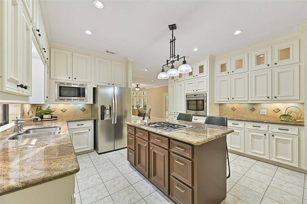 This beautiful island kitchen is accessible from both the dining room and the breakfast room and it showcases updates that include exotic granite countertops, a tile backsplash, recessed lighting, and 42-inch white cabinetry with under-cabinet task lighting.