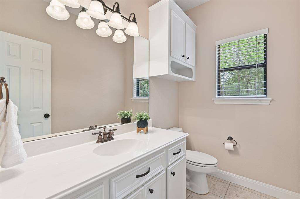Another half bathroom is located just off of the kitchen area, near the utility room. Here, you'll note a lengthy cultured marble countertop atop white cabinetry, tile floors, and stylish lighting.