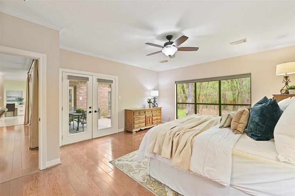 Escape to the first-floor owners' retreat that showcases more wood floors, a lighted ceiling fan, neutral paint trimmed with crown molding, an expansive rear-facing window with pleated shades, and French doors allowing a private exit to the covered patio area.
