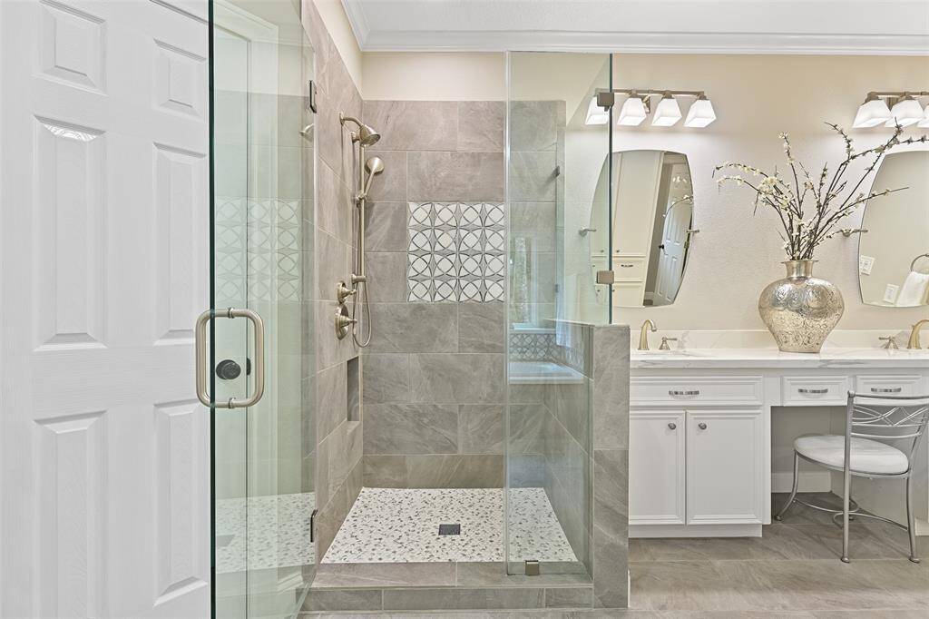 Relaxation awaits beneath the deep waters of this soaker tub with a modern tile surround that is also mimicked in the walls of the seamless glass shower. An undivided glass window with a deep ledge lets light in and looks out over the wooded side yard.