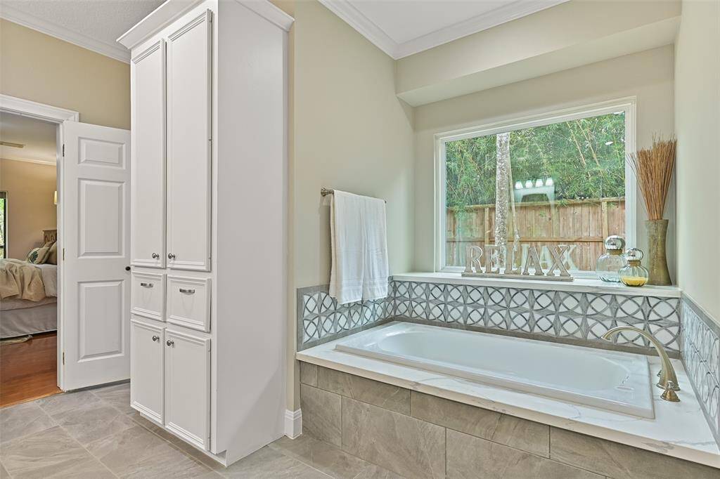 Relaxation awaits beneath the deep waters of this soaker tub with a modern tile surround that is also mimicked in the walls of the seamless glass shower. An undivided glass window with a deep ledge lets light in and looks out over the wooded side yard.