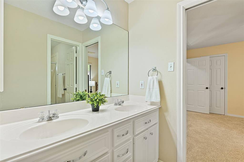 This Jack & Jill style bathroom services the secondary bedrooms and it features a cultured marble countertop with dual basin sinks, white cabinetry, tile floors, stylish lighting, a convenient laundry shoot, and a combination bathtub and shower with a glass door.