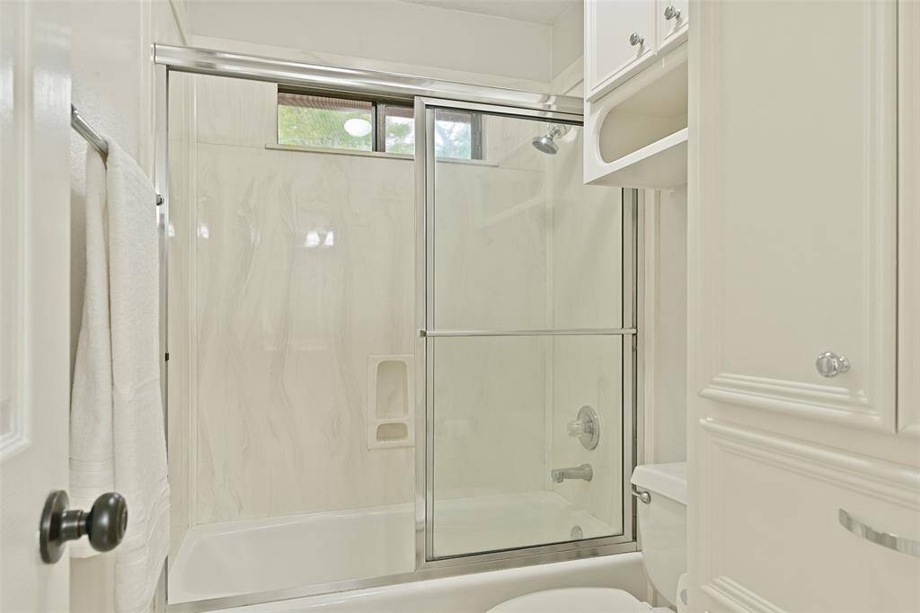 This Jack & Jill style bathroom services the secondary bedrooms and it features a cultured marble countertop with dual basin sinks, white cabinetry, tile floors, stylish lighting, a convenient laundry shoot, and a combination bathtub and shower with a glass door.