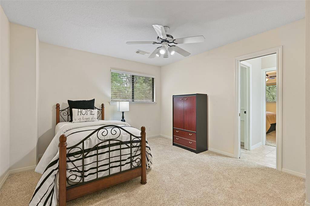 On the opposite side of the Jack & Jill style bathroom, this bedroom hosts a lighted ceiling fan, plush carpet, neutral paint, a side-facing window shaded by 2-inch blinds, and a spacious walk-in closet.