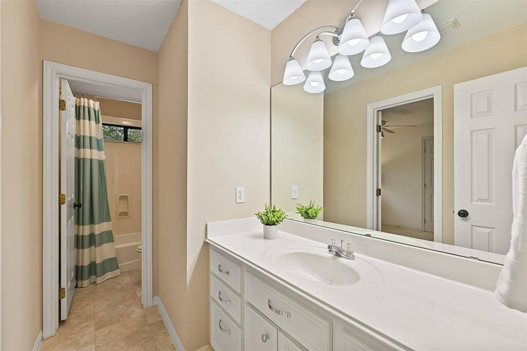 This Jack & Jill style bathroom services the previous bedroom and gameroom, offering a lengthy cultured marble vanity with a basin sink, white cabinetry, tile floors, updated lighting, and a combination bathtub and shower with a cultured marble surround.