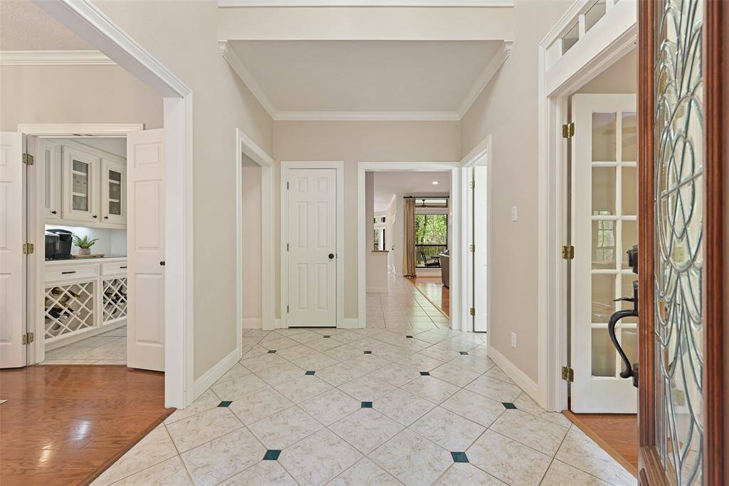 The covered front porch and leaded glass front door make way to this elegant foyer with a soaring two-story ceiling trimmed with ornate moldings, neutral paint, and tile floors, flanked by the dining room on the left and the study on the right.