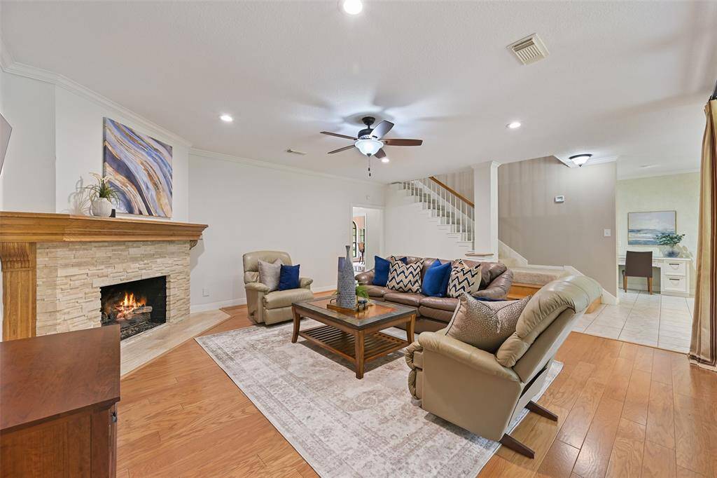 Continue straight ahead from the foyer into the heart of this home, where you'll find a spacious family room with warm wood floors, a lighted ceiling fan, recessed lighting, and a corner-set gas log fireplace with a stacked stone facade and a milled wood mantle.