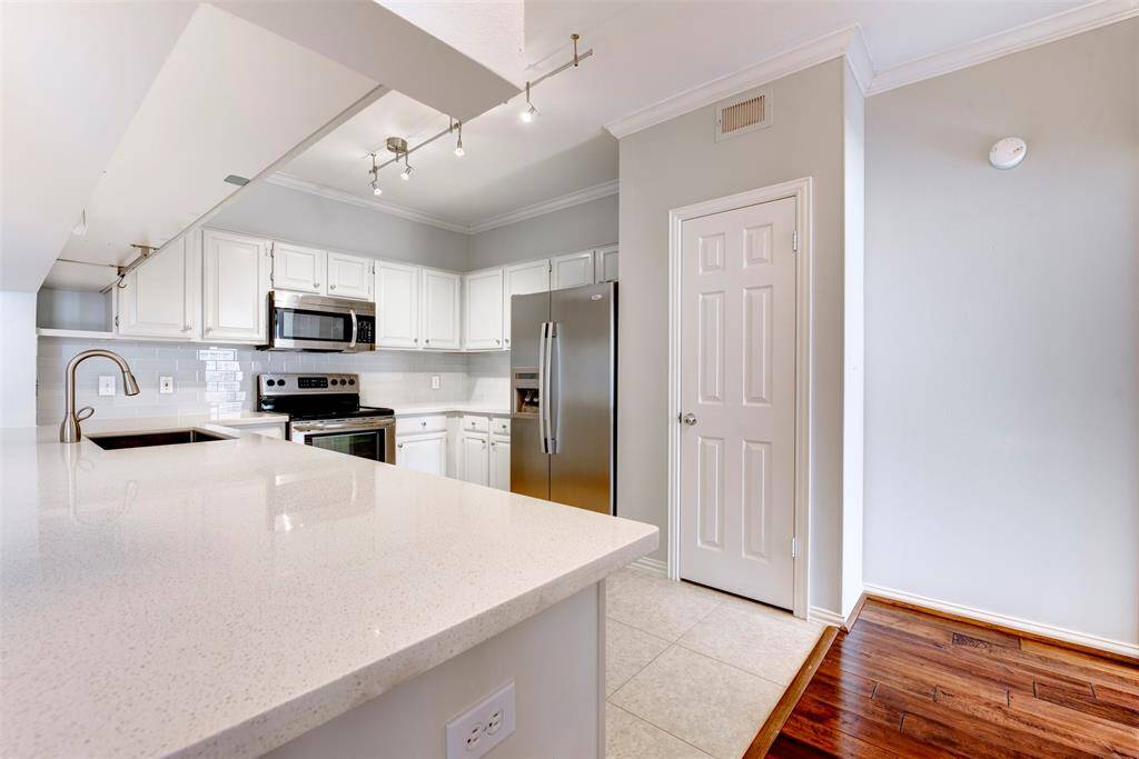 Bright and spacious kitchen with modern appliances, white cabinetry, and a mix of tile and hardwood flooring. Features sleek lighting and ample counter space, perfect for cooking and entertaining.