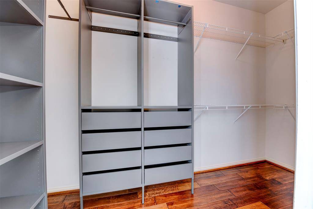 The primary suite offers a reconfigured walk-in closet with wooden floors, ample shelving, and hanging space, featuring both open shelves and drawers for organized storage.