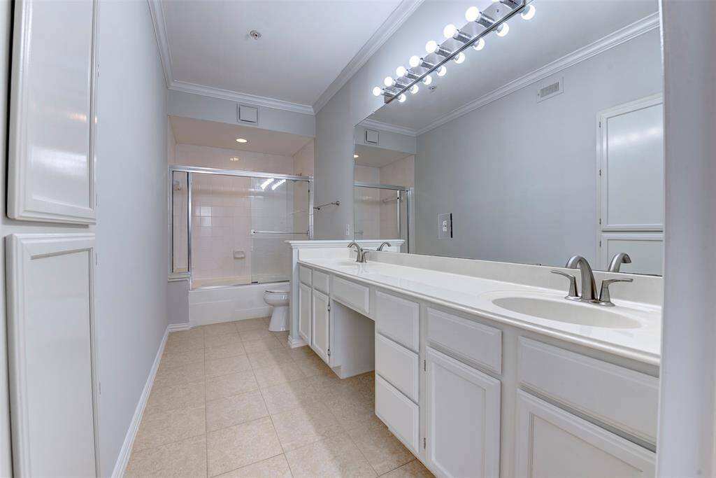 The primary bathroom features a clean, modern design with dual sinks, ample countertop space, and a large mirror. It includes a shower-tub combination with glass sliding doors and neutral tile flooring, creating a bright and spacious feel.