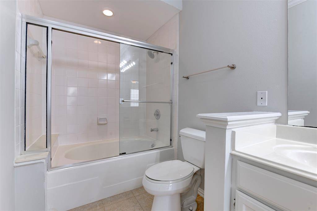 Alternate view of the clean, modern design with a bathtub and shower combo enclosed by sliding glass doors. It has a light color palette, and tiled walls.