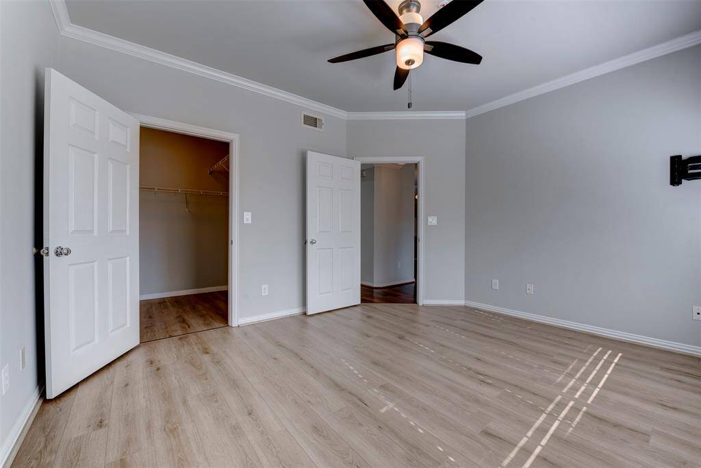 Bright bedroom with light wood flooring, neutral walls, and crown molding. Features a ceiling fan with light kit, and a large walk-in closet.