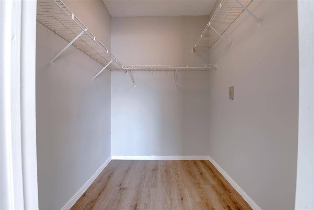 This photo shows a spacious walk-in closet with light colored walls, wood LVP flooring, and white wire shelving for ample storage.