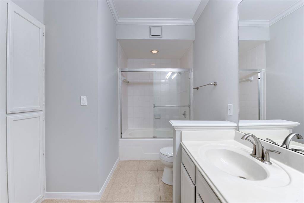 Alternate view of the modern design with light walls, a white vanity with an undermount sink, a large mirror, and a bathtub with a glass sliding door.