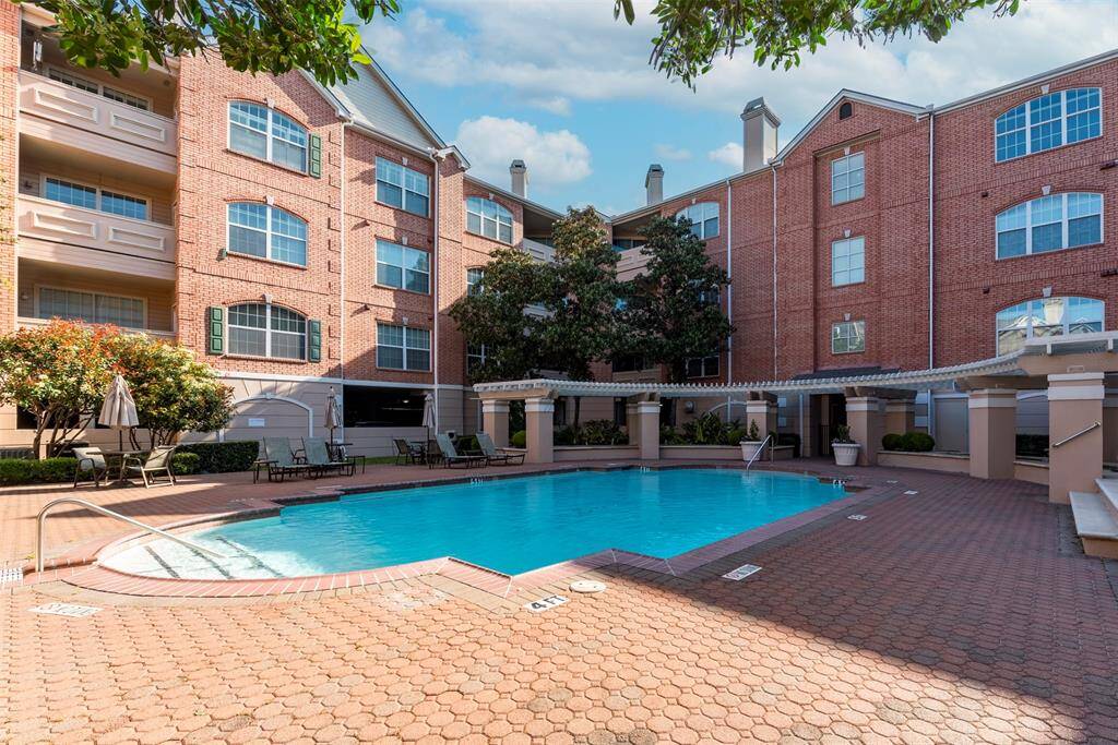 This photo showcases a well-maintained condominium courtyard with a spacious swimming pool surrounded by brick buildings. The area features poolside seating and lush greenery, creating a relaxing ambiance.