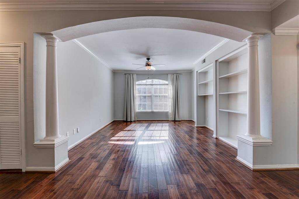 Bright and spacious living area featuring elegant columns, hardwood floors, built-in shelving, and large windows for natural light.