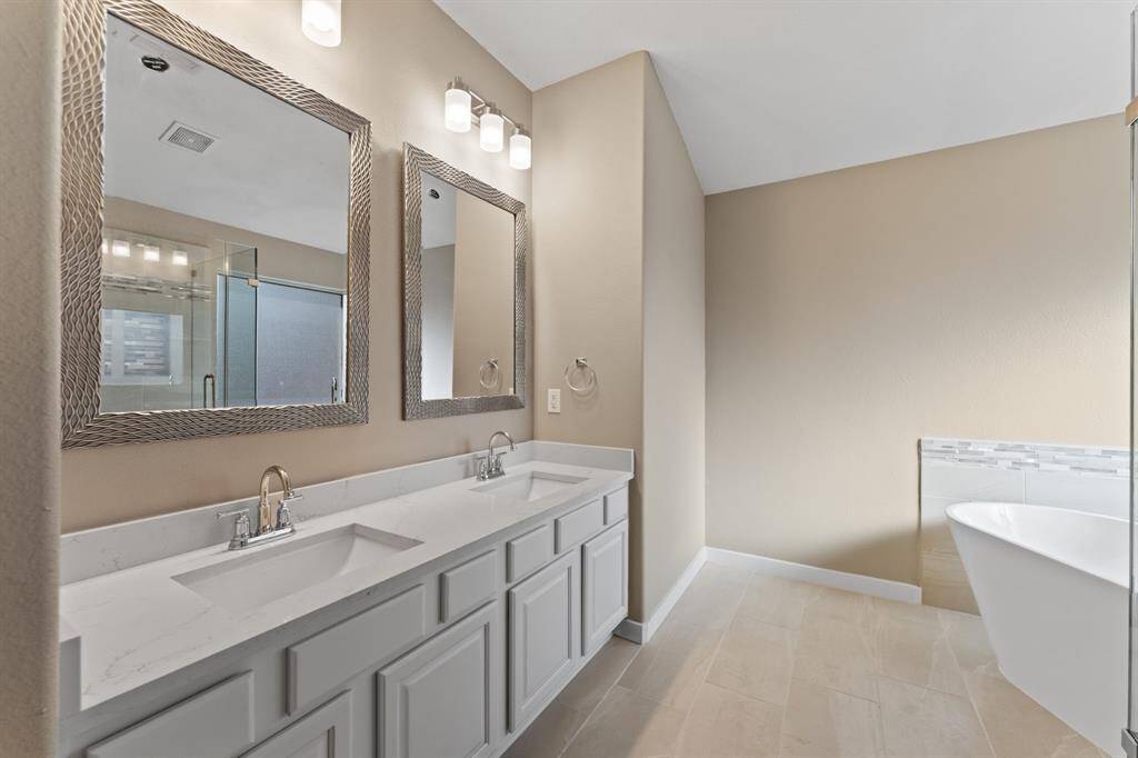 Primary bath has double sinks with framed mirror and decorative lighting.  Standalone soaking tub in the corner.