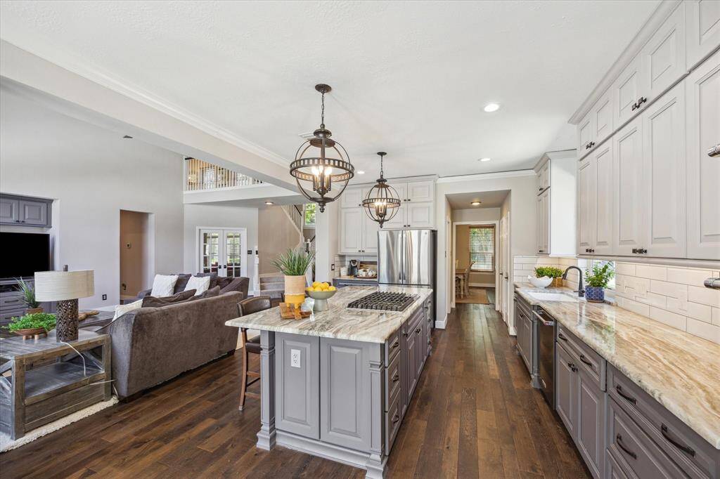 ALTERNATE VIEW OF THE KITCHEN/LIVING  Warm, wide plank hardwood flooring spans nearly all of the first floor.  Two toned cabinets feature darker nuetral paint on the lowers and a lighter coordinating color for rhe uppers.  At left a cordinating built in unit which houses the tv is both functional and aesthetically pleasing.